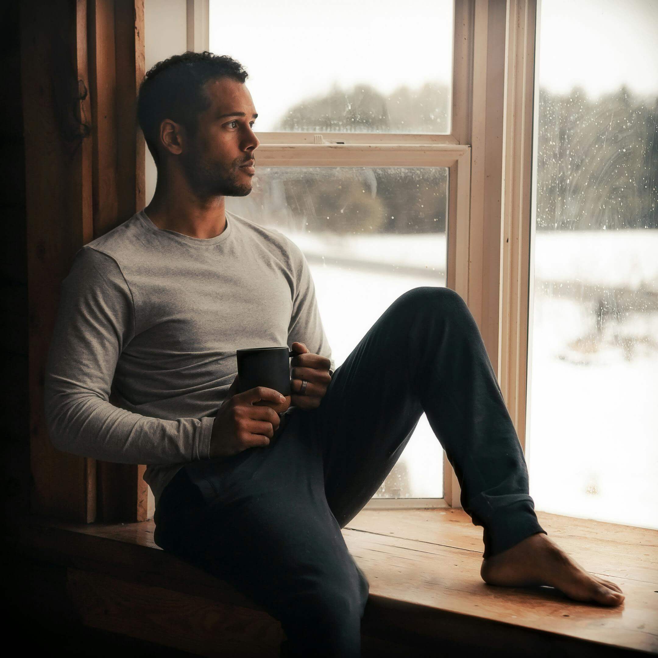 person sitting quietly by a window on a winter day reflecting and holding a warm mug